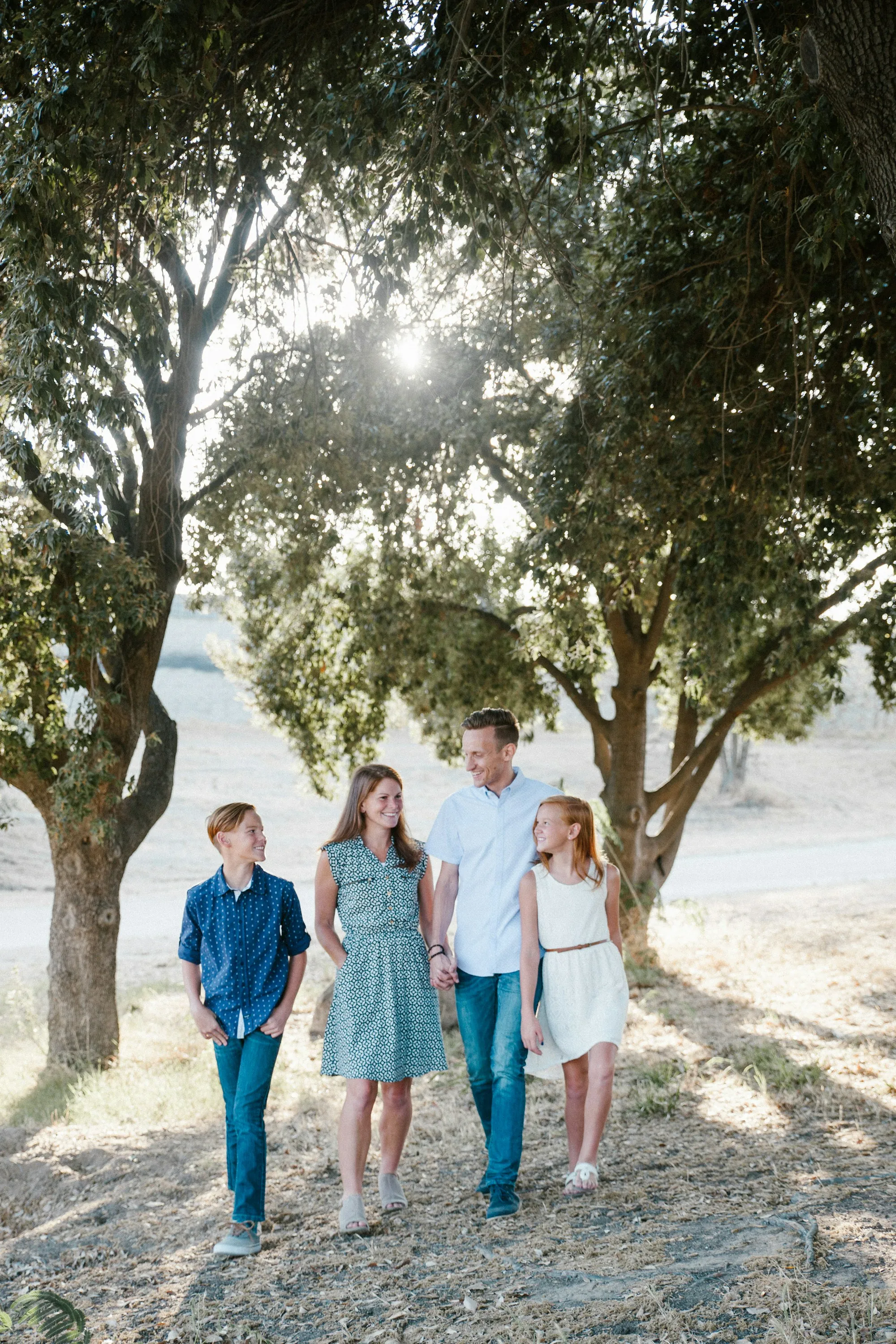 Parents and three children walking under trees by the water
